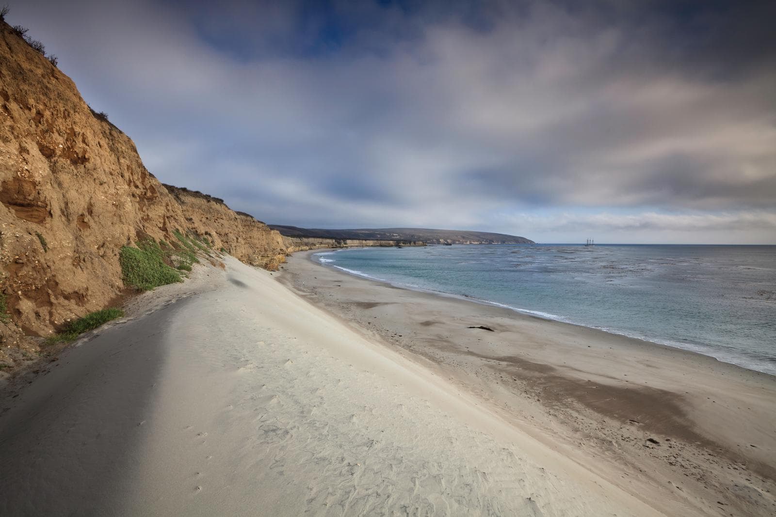 White sand dune next to a steep coastal bluff with ocean. 