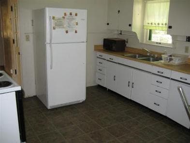 Kitchen with full size fridge with upper freezer, microwave next to metal sink with dish rack across from electric stove.