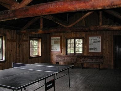 Ping-pong table in dimly lit large room with log rafters and benches.