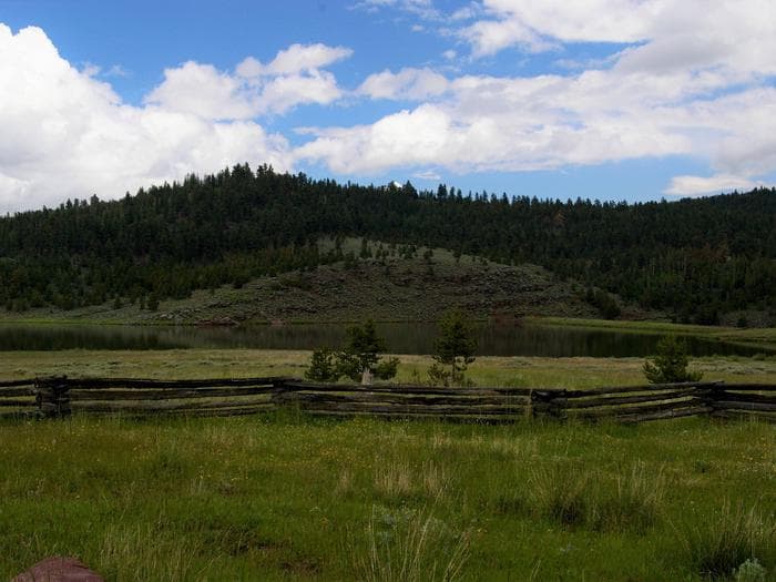 Browne Lake with the mountains in the background and a wooden fence in the foreground.
