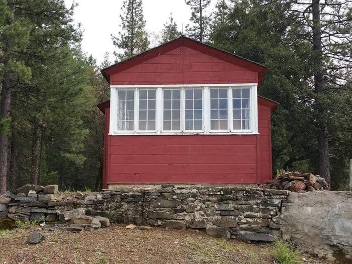 Back view of historic Post Creek Guard Station, red cabin, with white trim around windows.