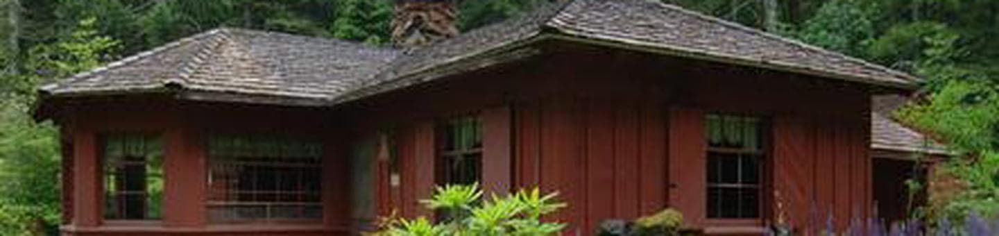 Cabin with red siding in front of conifer forest