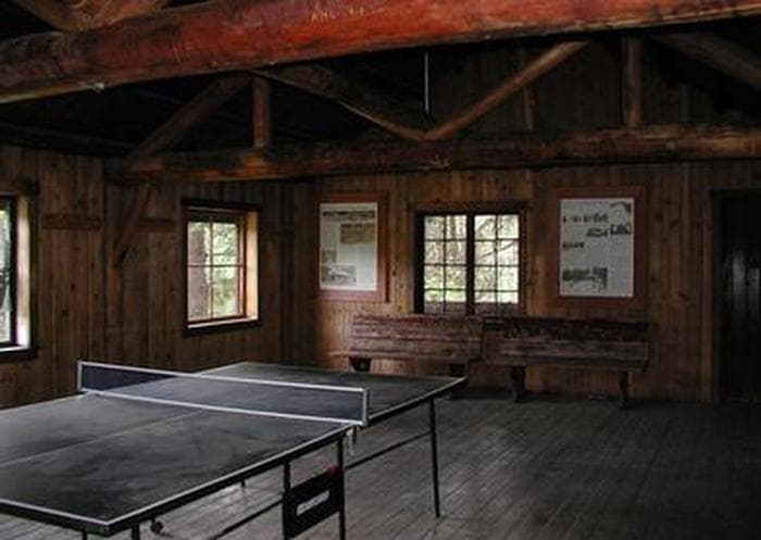 Ping-pong table in dimly lit large room with log rafters and benches.
