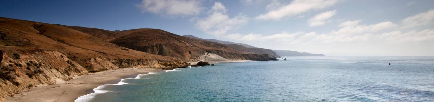 Sandy beach with ocean and small waves and steep coastal bluffs covered in dry grass