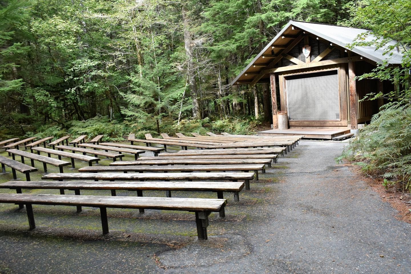 Rustic amphitheater in campground with benches and a building with a stage.