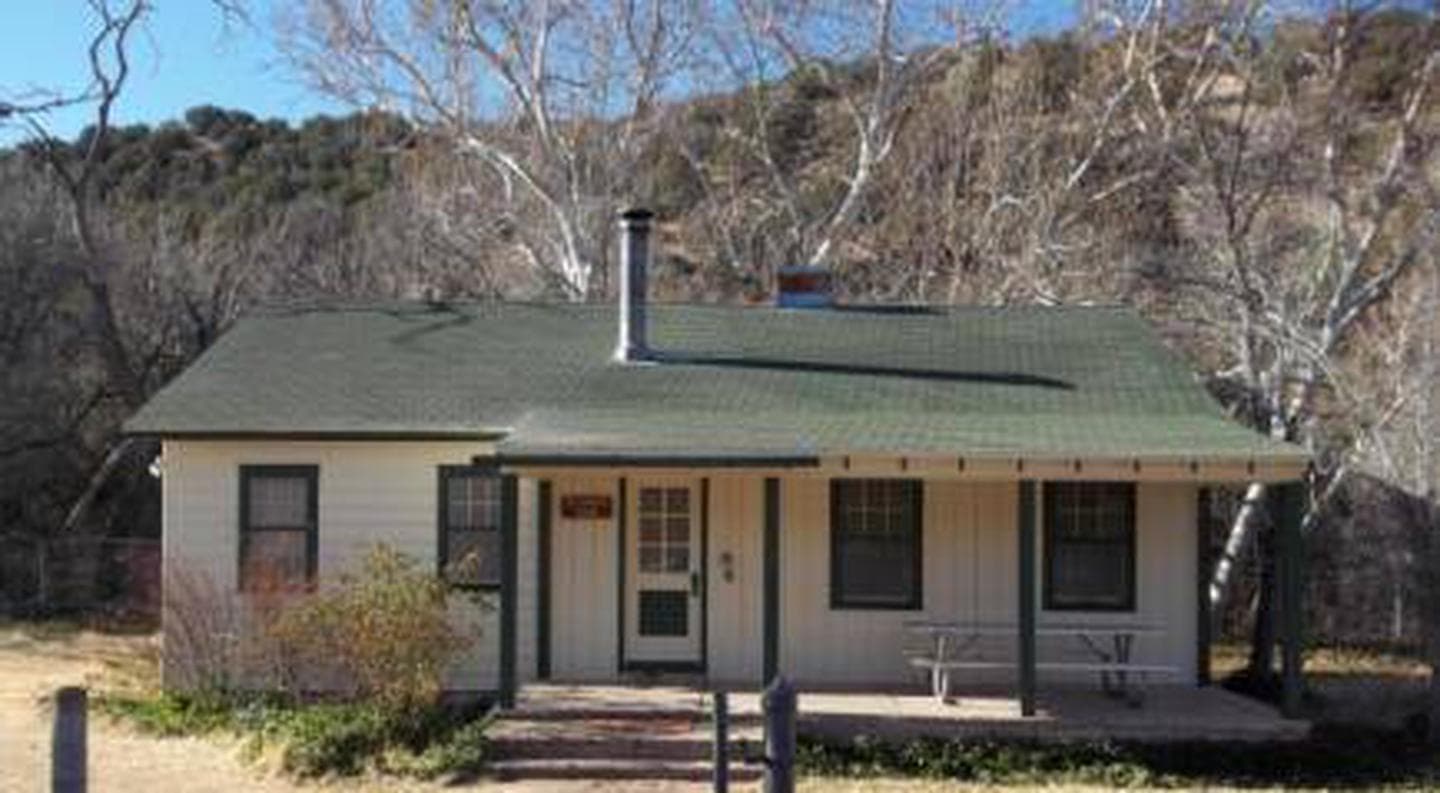 White exterior of Sycamore Cabin with a green roof, three stairs of different depths to porch with picnic table to right of door.