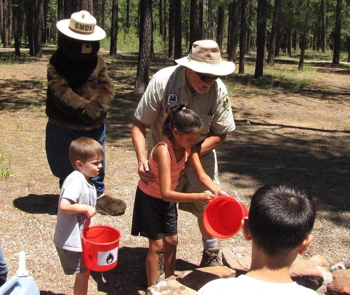 Smokey Bear oversees as children learn how to extinguish a campfire