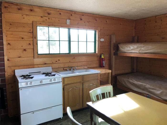 Cabin interior showing gas range, bunkbeds, table and dry sink