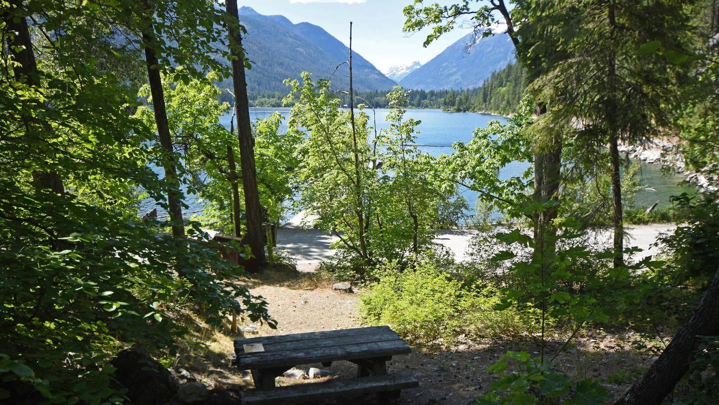 Picnic table with trees, lake, and mountains in the background.