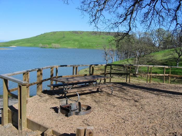Campsite within Buckhorn Campground showing picnic table, firepit, and lake in background.