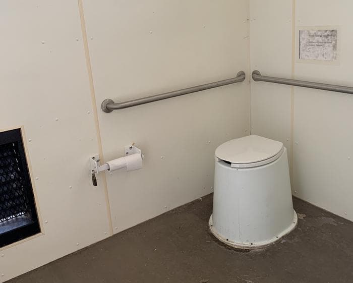 A toilet in the pit toilet building with rolls of toilet paper on the left.