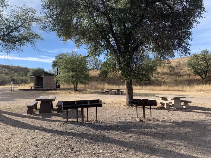 Campground with tables, grills and a pit toilet. Sparse trees and a dry, grassy ecosystem