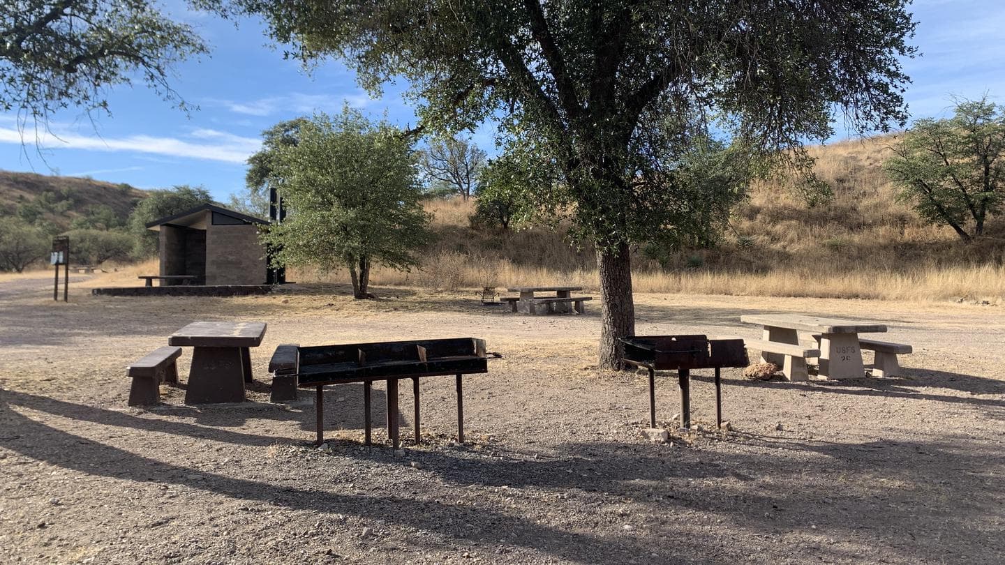 Picnic tables, grills and a pit toilet at the central area of the Calabasas campground.