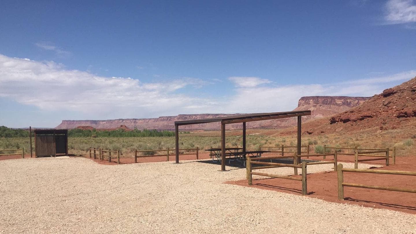 Superbowl group site shad structure and vault toilet with scenic red sandstone cliffs in background.