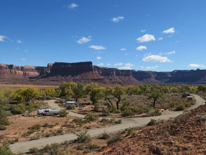 A gravel campground loop road surrounded by Cottonwood trees with red sandstone cliffs in background.