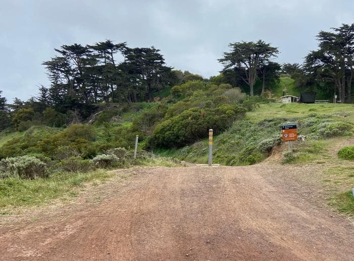 A dirt road leads down to Bicentennial. Battery Wallace with picnic tables and a vault toilet is in the background.