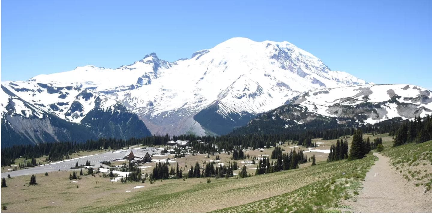 A panoramic view hiking on trail above the subalpine meadows of Sunrise with Mount Rainier in the background.