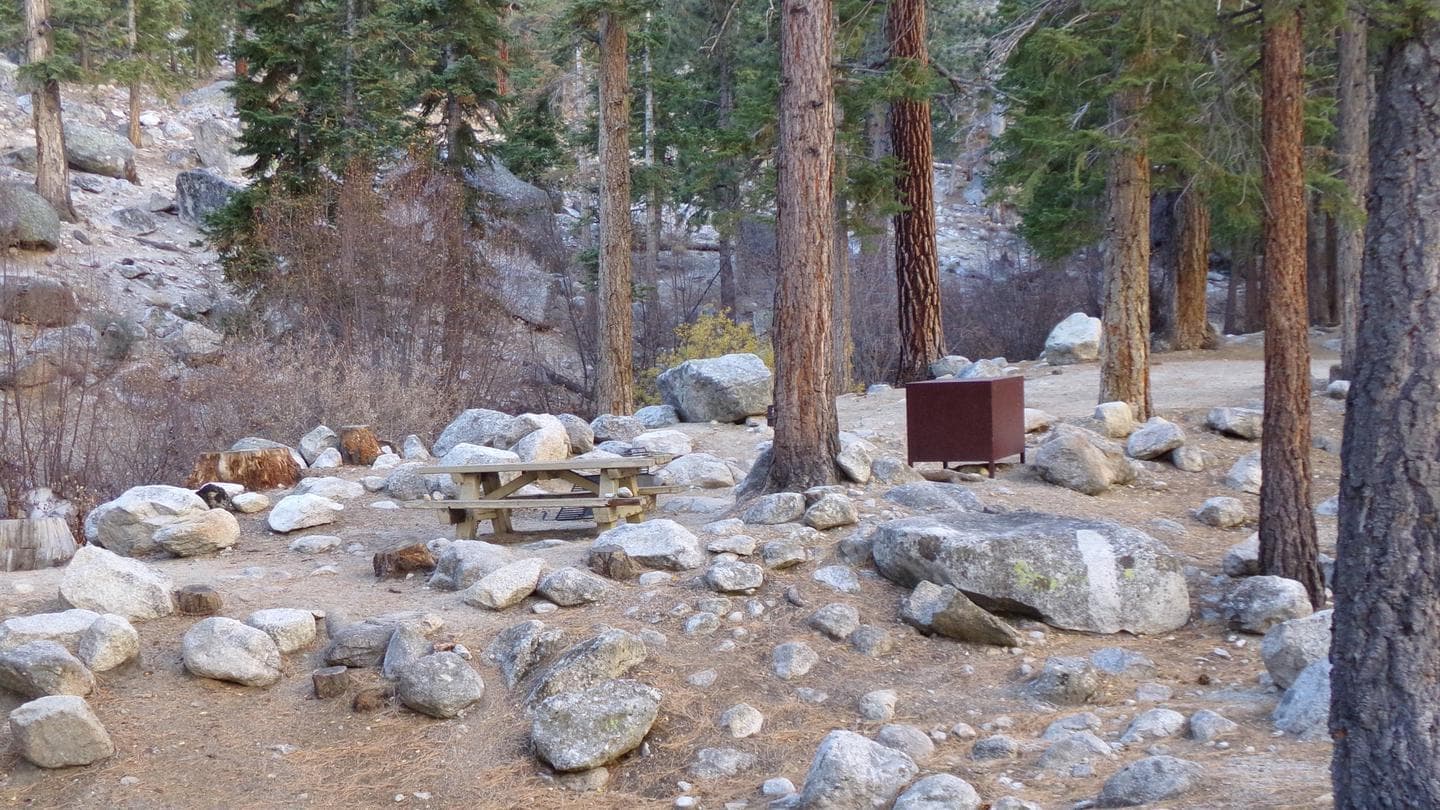 A Whitney Portal campsite with picnic table and bear box, nestled between boulders and near a creek.