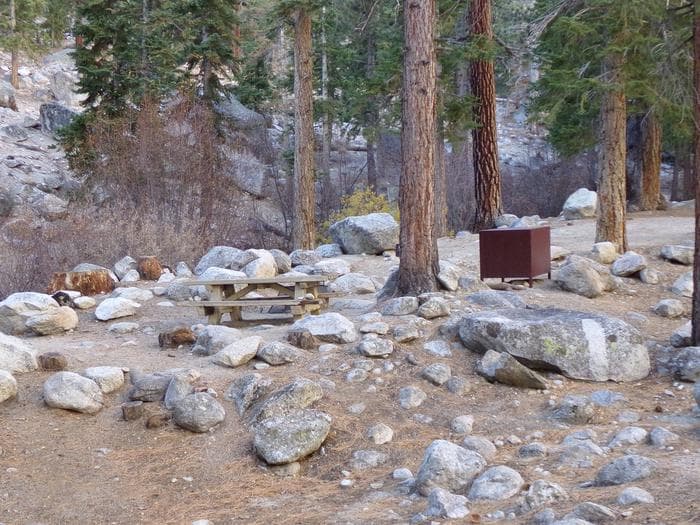 Campsite at Whitney Portal campground located near a creek amongst boulders. The campsite offers a picnic table and bear box.