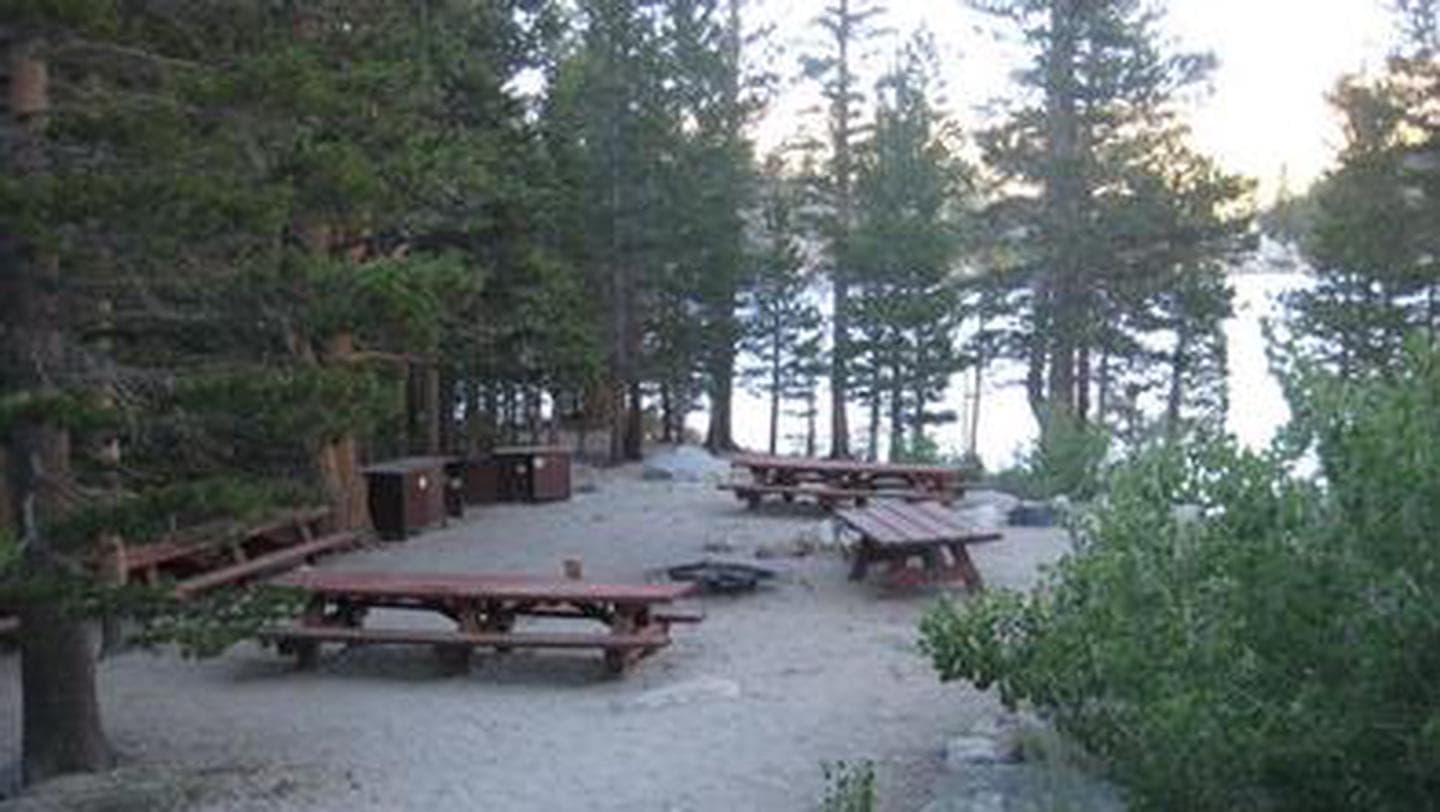 Several picnic tables around a fire ring on a cliff near a lake