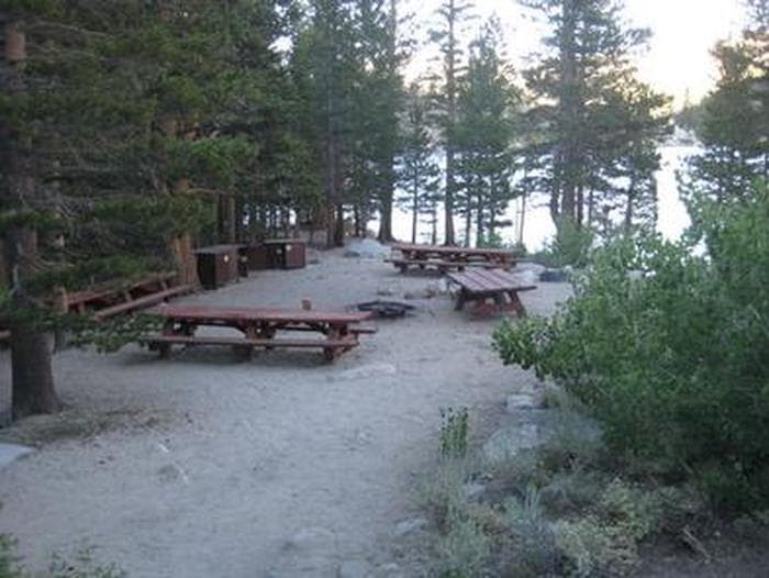 Several picnic tables around a fire ring on a cliff near a lake
