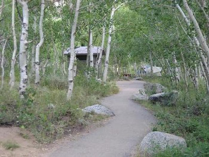 A path winds through trees towards a restroom facility