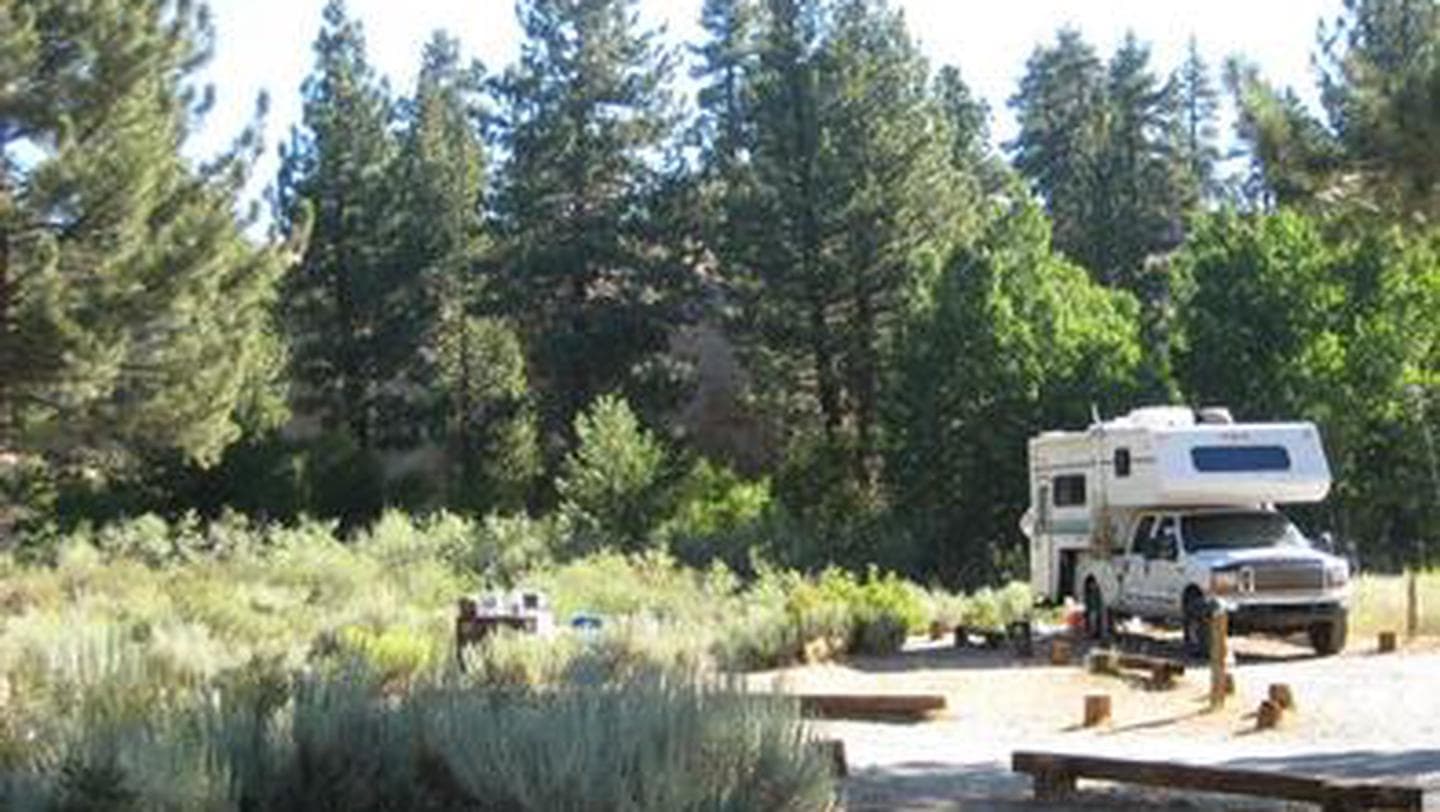 A pickup truck with an attached camper parked at a dirt campsite