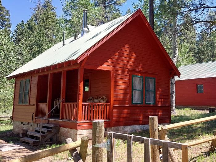 A sunny day illuminates Patterson Guard Station. The bright red color of the Guard Station contrasts the green conifer trees behind it.
