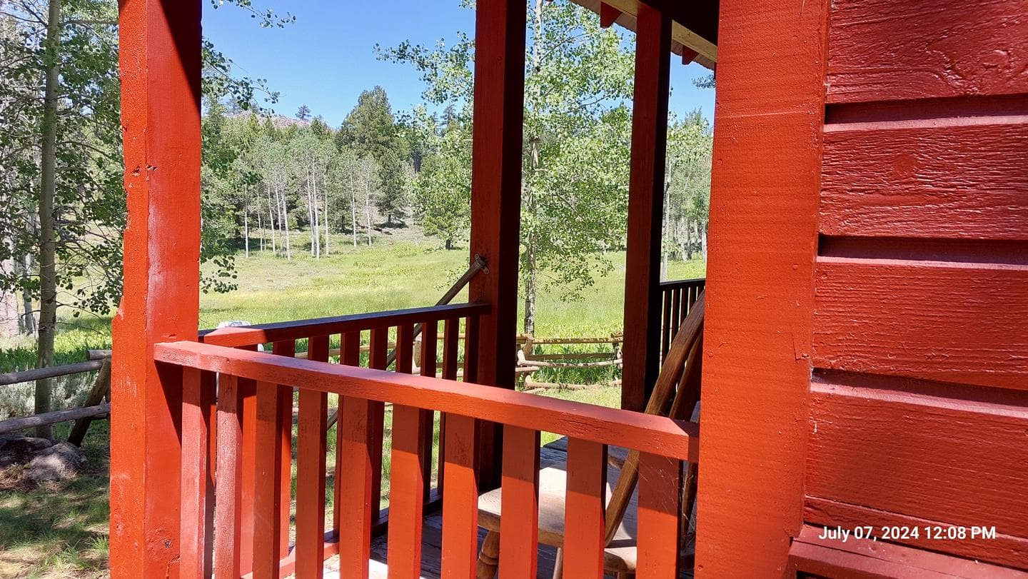 bright red wooden rails frame the front porch of the guard station where a wooden chair offers a view of the adjacent meadow on a sunny day.