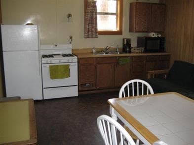 Kitchen with table, medium fridge and upper freeze next to electric stove, microwave and coffee maker on counter.